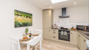 A modern kitchen with a dining area, featuring a painting, a microwave, and a sink. - Cosy historic cottage in Hillsborough, near Belfast, Dublin & local attractions (Royal Hillsborough)