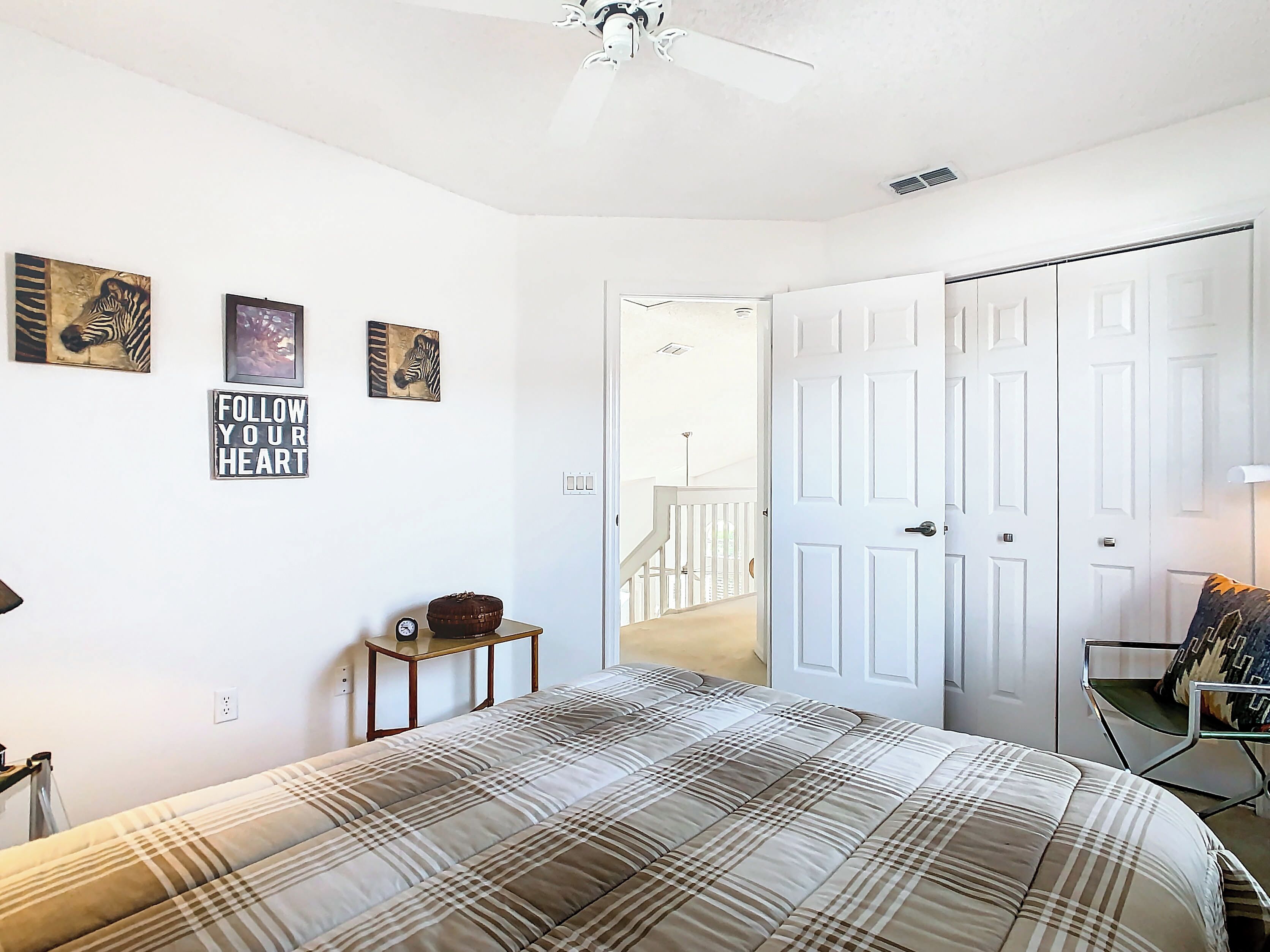 A bedroom with a bed, a bedside table, a chair, and a door leading to another room.