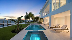 Uma área de piscina moderna com vista para o oceano, cercada por palmeiras e espreguiçadeiras.
