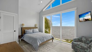 Quarto com uma cama grande, vista para a praia e televisão na parede.