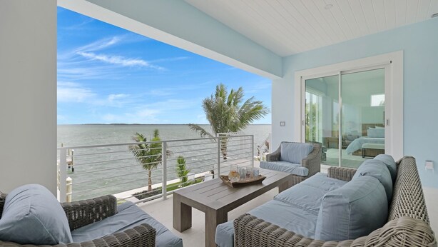 Uma varanda com móveis de vime, uma mesa e vista para o mar.