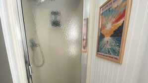 Una ducha con cerramiento de vidrio y estructura de madera, una alfombra azul y un cartel en la pared.