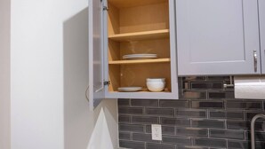 Eine Küche mit grauen Schränken, einem Holzregal und einer schwarzen Küchenrückwand.