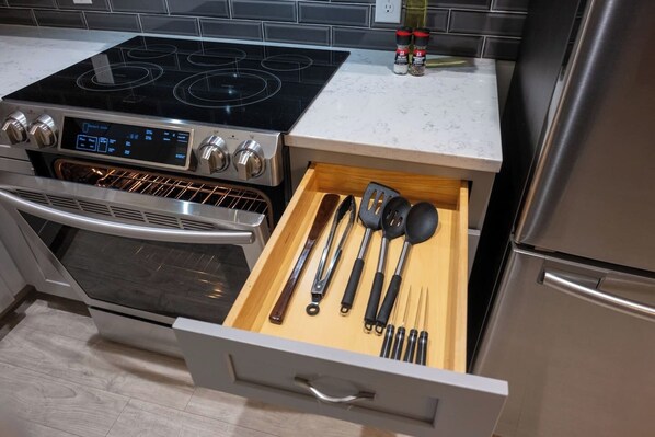 Cocina con estufa, horno y cajón con utensilios.