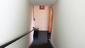 A staircase with a handrail, a fire alarm, and a wooden door at the bottom. - Hoosier Suite Modern Studio Downtown on the Square (Bloomington)
