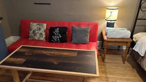 A room with a red sofa, a wooden coffee table, a lamp, and a small wooden side table. - Maryland Homestay - Downtown Apartment #1 (Winnipeg)