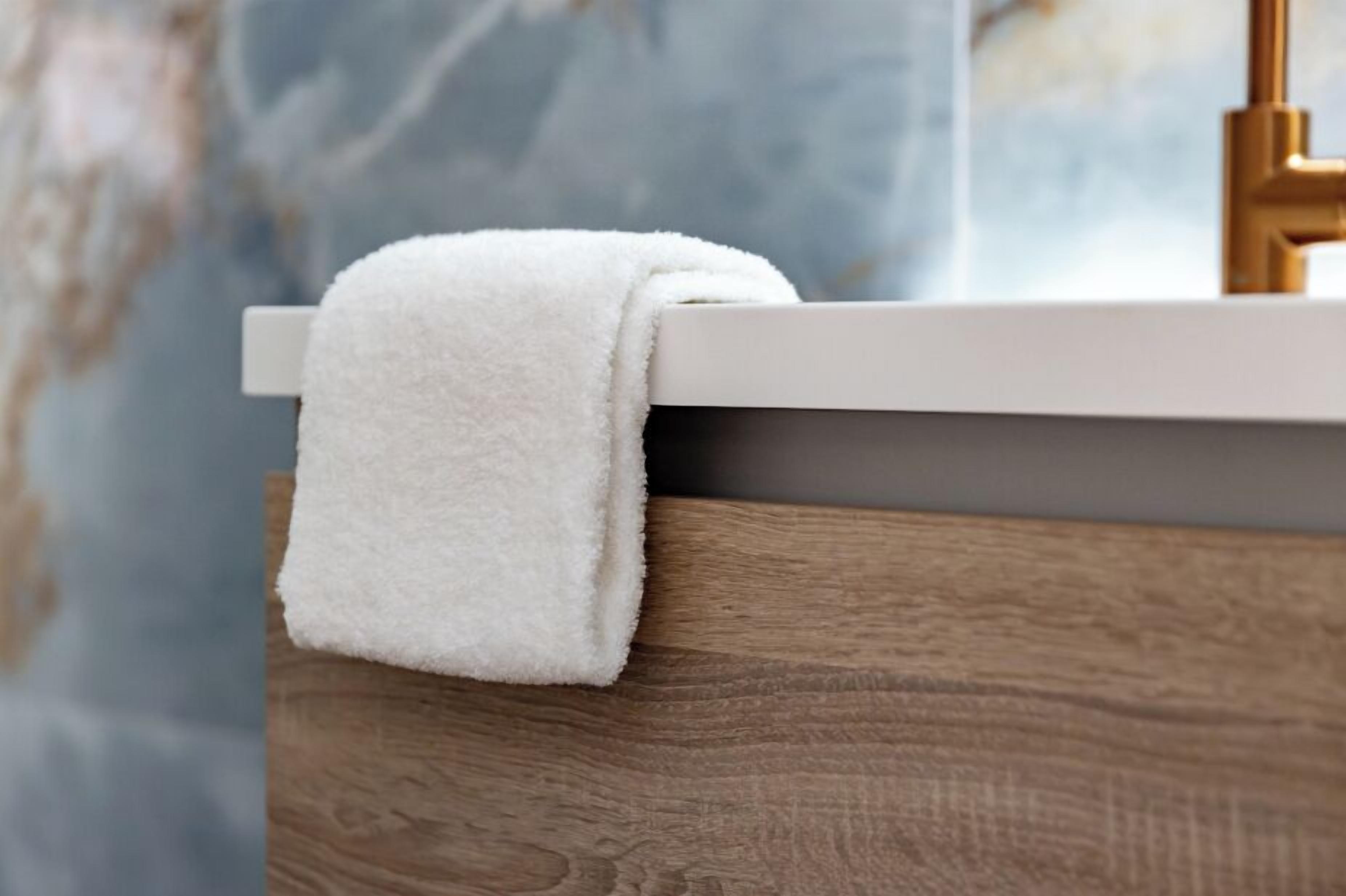 Una toalla blanca colgada en un toallero de madera en un baño con una pared de mármol al fondo.