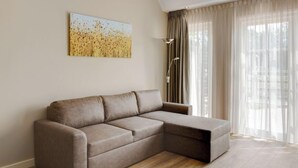 Ein modernes Wohnzimmer mit einem Ecksofa, einer Stehlampe und einem großen Fenster mit durchscheinenden Vorhängen.