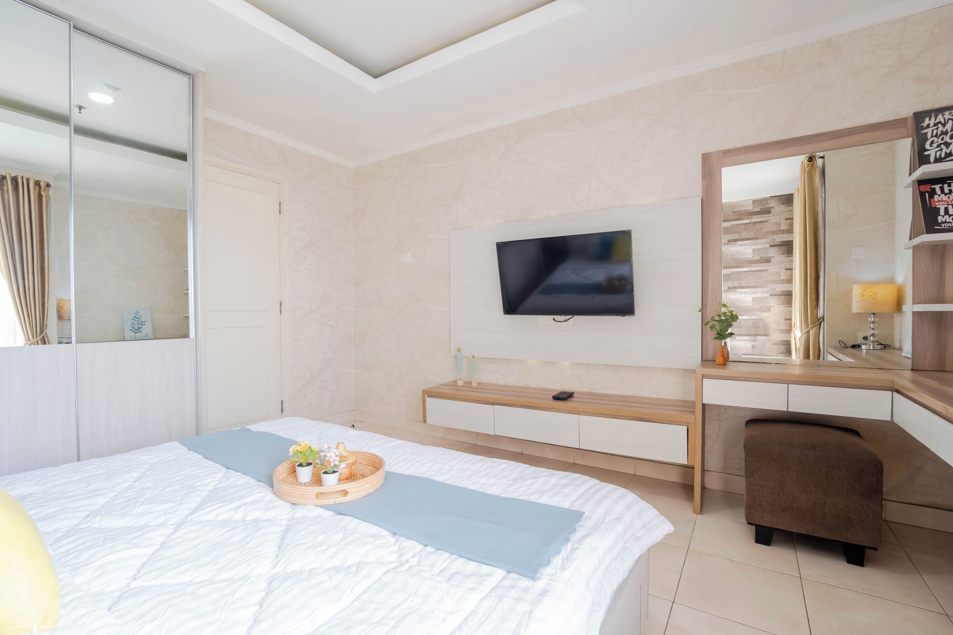 A modern hotel room with a large bed, a flat-screen TV mounted on the wall, a wooden desk, and a small seating area.