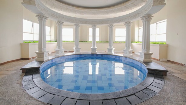 A circular pool with blue tiles surrounded by white columns and a curved ceiling. - The Boulevard Apartment By Abdihome (Jakarta)