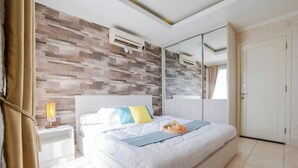 A modern bedroom with a large bed, a nightstand with a lamp, a wall-mounted air conditioner, and a sliding door closet. - The Boulevard Apartment By Abdihome (Jakarta)