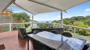 A covered outdoor seating area with a glass table and chairs, overlooking a scenic view of the ocean and lush greenery. - Sundowner is the perfect escape for a relaxing holiday (Point Lookout)