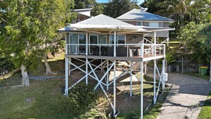 A two-story house with a deck, surrounded by trees and a clear sky. - Sundowner is the perfect escape for a relaxing holiday (Point Lookout)