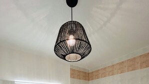A modern bathroom with a white vanity, a large mirror, a black pendant light, and a bathtub with beige tiles.