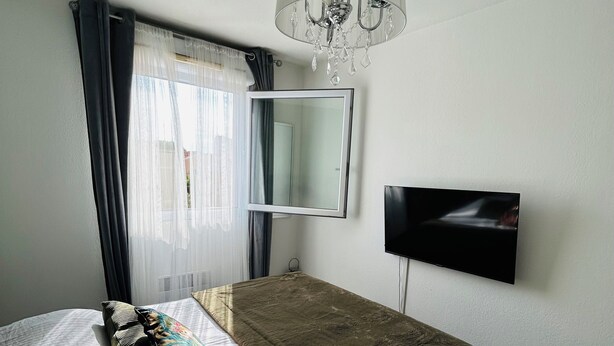 A bedroom with a bed, a mirror, a TV, and a chandelier.