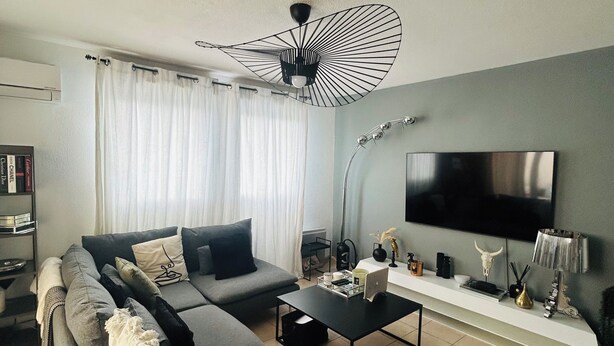 A modern living room with a sectional sofa, a coffee table, a flat-screen TV, and a ceiling fan.