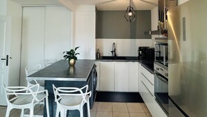 A modern kitchen with white cabinets, a central island with chairs, a ceiling fan, and a stainless steel refrigerator.