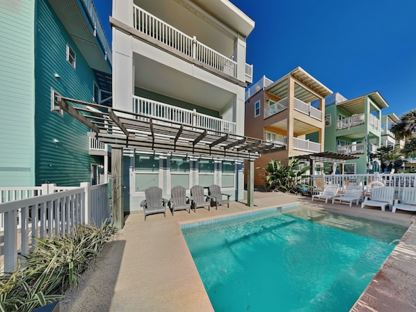 A pool area with lounge chairs and a pergola, surrounded by multi-story buildings with balconies.