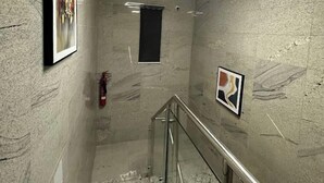 Un passadís amb parets de marbre, barana de vidre i quadres emmarcades.