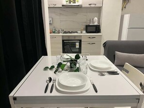 A dining table set with plates, cutlery, and glasses in a modern kitchen with a microwave and stove.