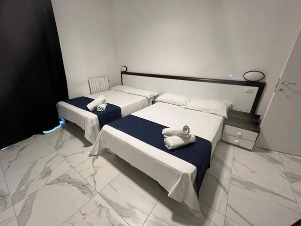 A hotel room with two single beds, a nightstand, a dresser, and a bathroom door.