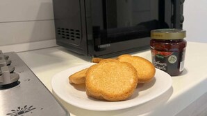 Keittiön työtasolla on leivänpaahdin, lautasella kaksi paahtoleipäviipaletta ja purkki mansikkahilloa.