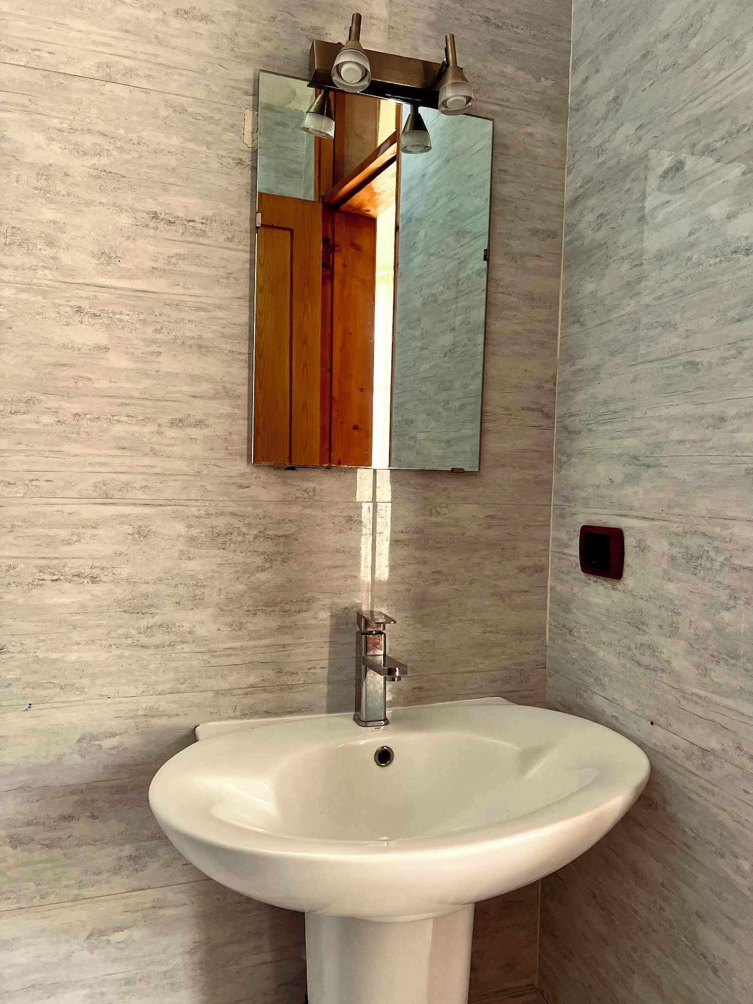 Une salle de bain avec un lavabo blanc, un miroir et un luminaire.
