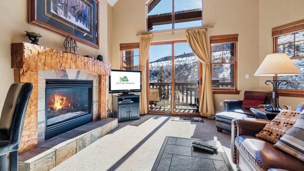 A cozy living room with a fireplace, a television, and a view of a snowy landscape through large windows. - Entire condo in Avon, Colorado (Avon)
