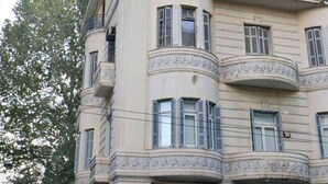 Un immeuble à plusieurs étages doté d’une façade incurvée, de balcons avec des garde-corps noirs et de nombreuses fenêtres.