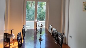 Une salle à manger avec une longue table, des chaises, un lustre et une fenêtre donnant sur un paysage verdoyant.