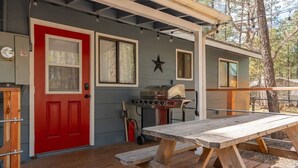 A wooden deck with a picnic table, a red door, and a barbecue grill.