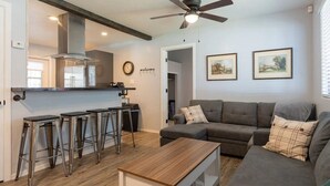 A modern living room with a grey sofa, a wooden coffee table, and a bar area with stools.