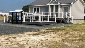 A small, single-story building with a grey roof and white trim, featuring a porch with white railings and a small staircase. - Near Chincoteague & Assateague Island
Charming 2-bedroom cottage (Saxis)