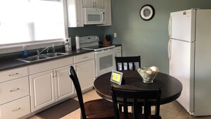 A kitchen with white cabinets, a microwave, a refrigerator, a sink, and a dining table with chairs. - Near Chincoteague & Assateague Island
Charming 2-bedroom cottage (Saxis)