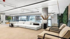 A modern lobby with a white sofa, beige chairs, and a large window. - Stunning Flat swimming pool/gym (London)