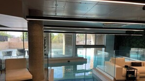 A modern indoor pool area with glass walls, a lounge chair, and a sofa. - Stunning Flat swimming pool/gym (London)