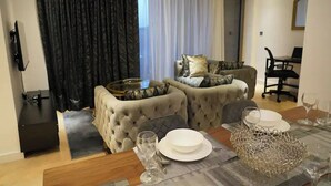 A modern living room with a sofa set, a dining table with plates and glasses, and a TV mounted on the wall. - Stunning Flat swimming pool/gym (London)