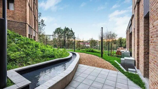 A courtyard with a water feature, brick buildings, and a pathway. - Stunning Flat swimming pool/gym (London)