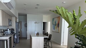 Eine moderne Küche mit Edelstahlgeräten, ein Essbereich mit einem Glastisch und ein Wohnzimmer mit grauem Sofa.