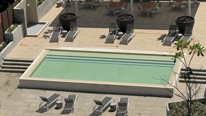 Ein Poolbereich auf dem Dach mit mehreren Liegestühlen, einem zentralen Pool und umliegenden Kübelpflanzen.