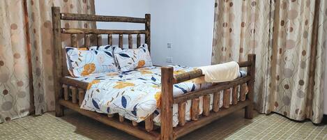 Una cama de madera con una colcha y almohadas estampadas con motivos florales, un cabecero de madera y cortinas con un diseño circular.