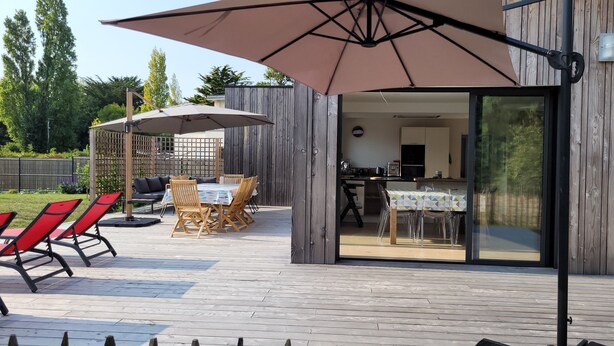 An outdoor patio with a wooden deck, a table with chairs, and a large umbrella providing shade. - Contemporary home in a quiet location, a 10-minute walk from the beaches (Loctudy)
