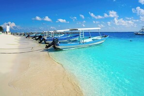 Uma praia com vários barcos atracados na margem, um céu azul límpido e uma faixa de areia.