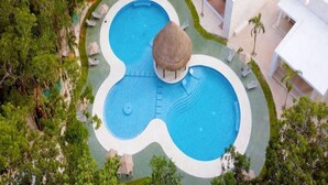 An aerial view of a resort with a large, uniquely shaped swimming pool surrounded by lounge chairs and a thatched-roof structure.