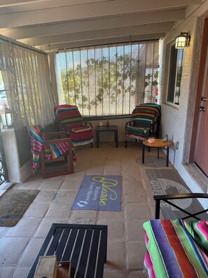 A covered porch with two chairs, a small table, a doormat, and a lantern.