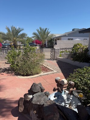 A paved driveway with a decorative stone sculpture, a gated entrance, and a building with a white exterior and gray roof.