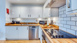 A modern kitchen with white cabinets, a stainless steel dishwasher, a wooden countertop, and a built-in oven.