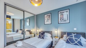 A modern bedroom with two beds, a large mirror, and artwork on the walls.