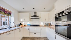 Una cocina moderna con armarios blancos, una campana extractora de acero inoxidable, un horno empotrado y una ventana con vista a un edificio de ladrillo.