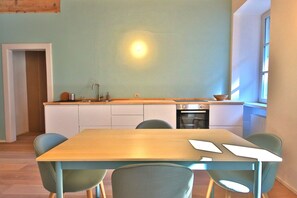 Cocina moderna con armarios blancos, encimera de madera y horno empotrado. En primer plano, hay una mesa de comedor con sillas.